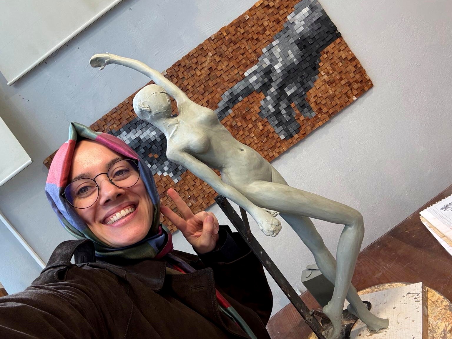 The artist smiling beside her clay dancing figure sculpture