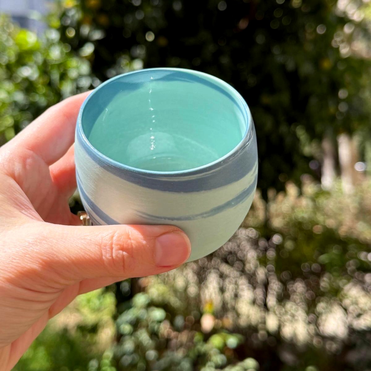 Handmade soft celadon tea cup held in sunlight